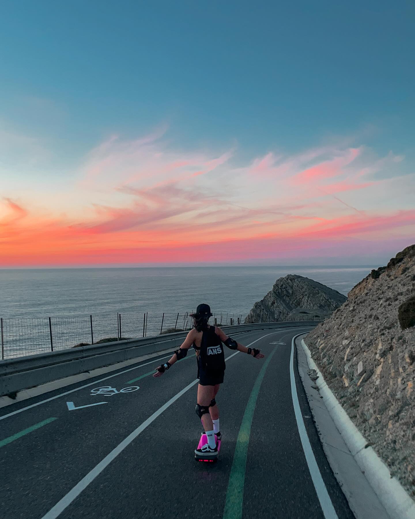 Riding a Onewheel on a road overlooking the ocean and sunset
